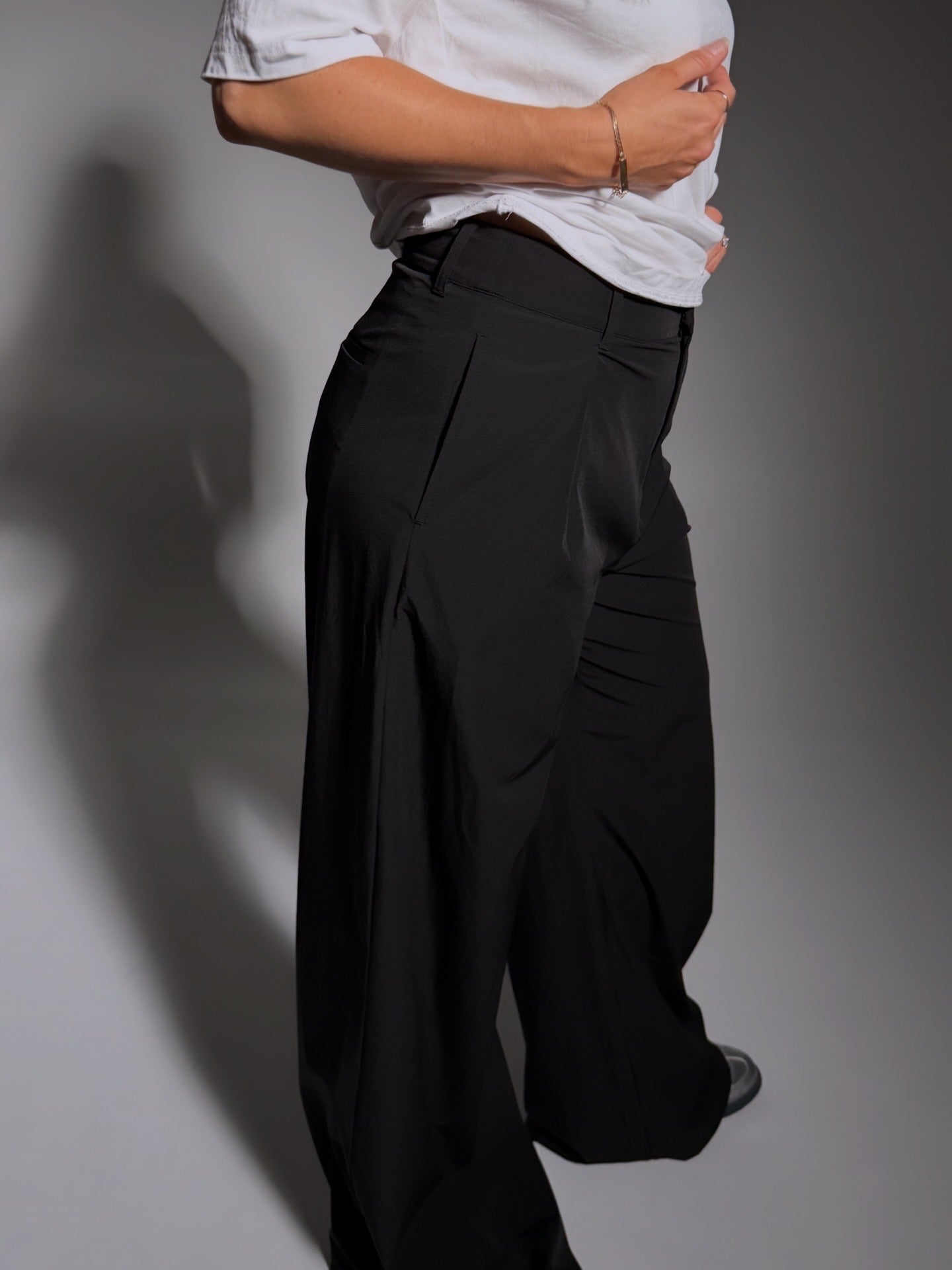 Person wearing a white shirt and black wide-leg pants against a gray background