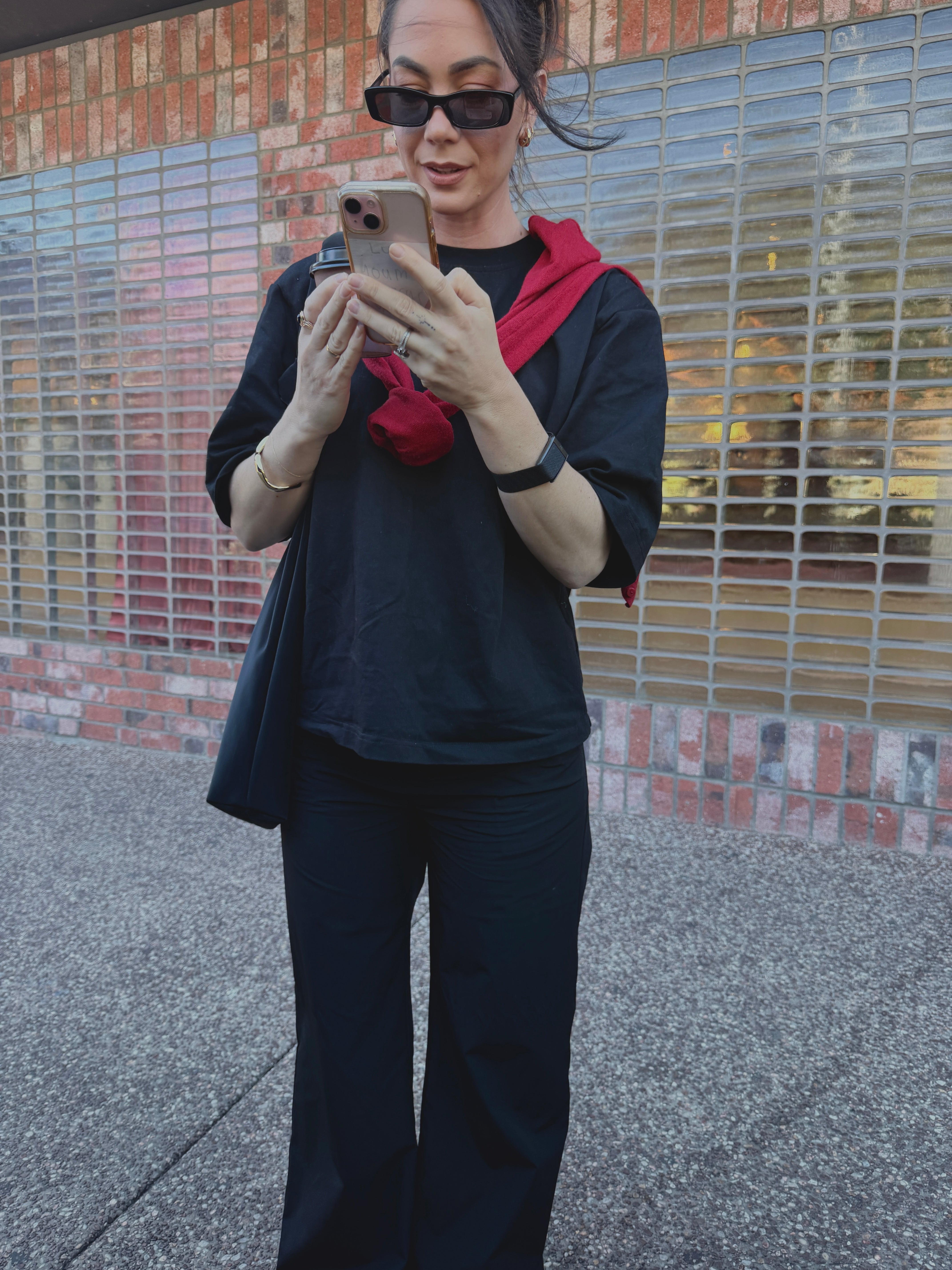 Woman talking on her phone outdoors, wearing sunglasses and the black tailored drew pants with a red scarf.