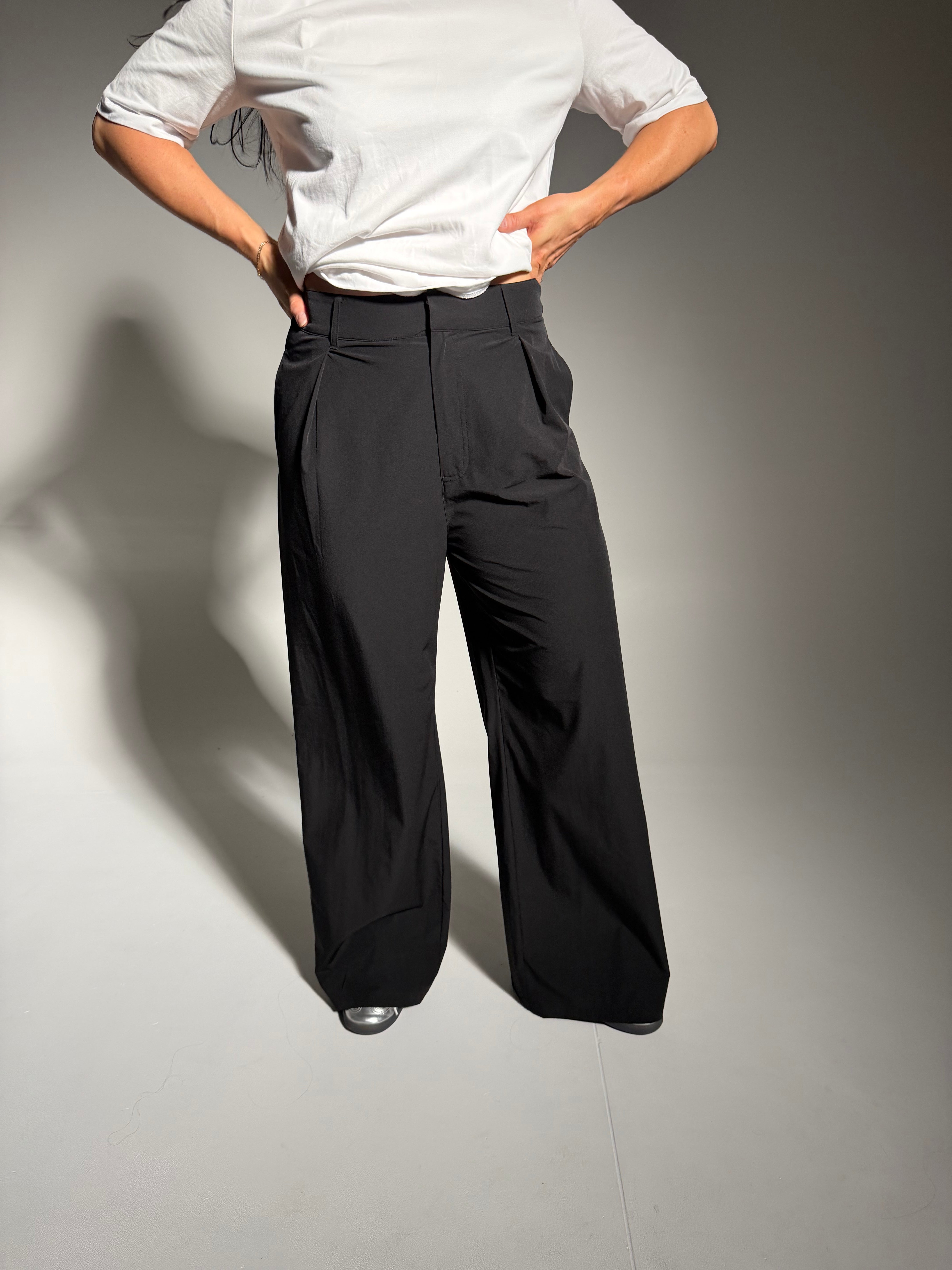 Person wearing a white shirt and black pants against a gray background