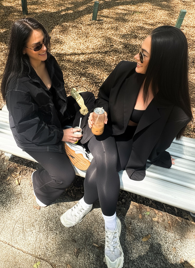 two active woman sitting in the park enjoying a coffee together, one of the woman is wearing the mack jacket by Noa Rae. 